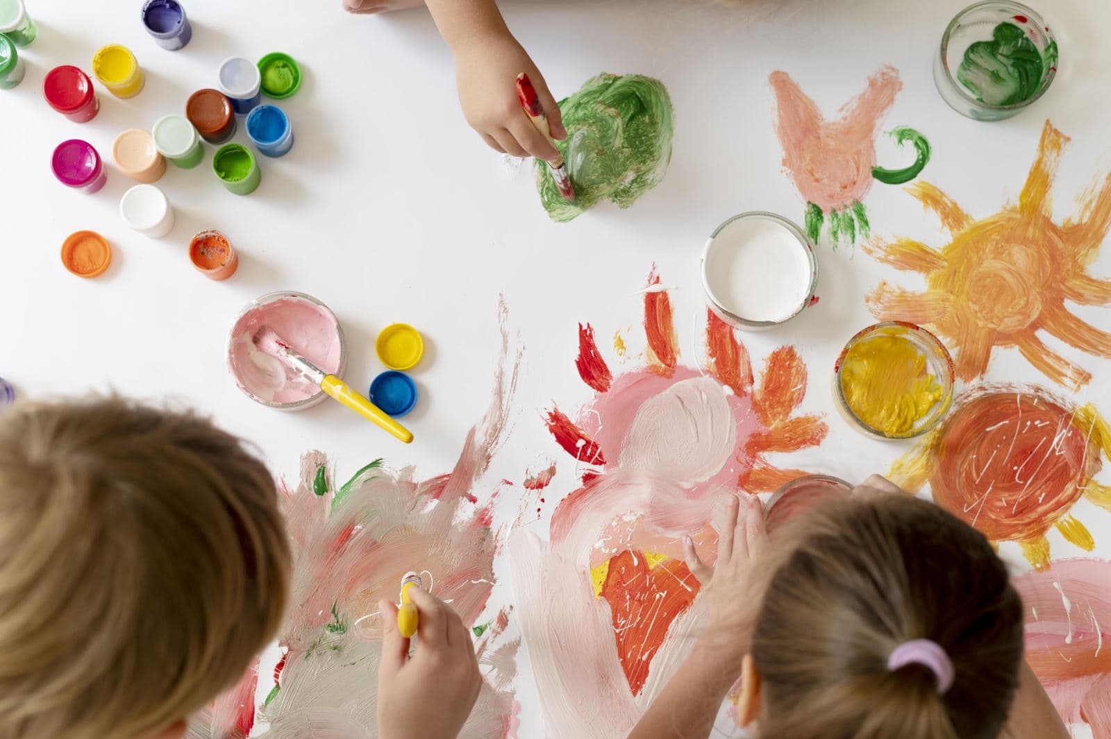 Duas crianças a pintar em conjunto numa mesa cheia de tintas coloridas